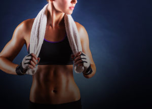 Young woman in workout grear, with towel around her shoulders after just finishing a workout